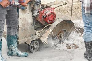 trabajador que utiliza una máquina de hoja de sierra de diamante cortando una carretera de hormigón en el sitio de construcción foto