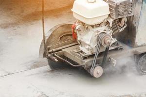 Worker using diamond saw blade machine cutting concrete road at construction site photo