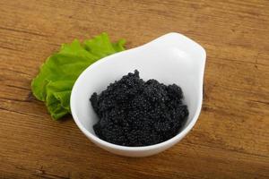 Black caviar in a bowl on wooden background photo