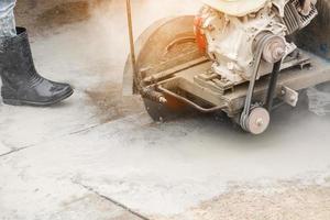 Worker using diamond saw blade machine cutting concrete road at construction site photo