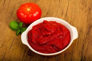 Tomato paste in a bowl on wooden background photo