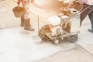 Worker using diamond saw blade machine cutting concrete road at construction site photo