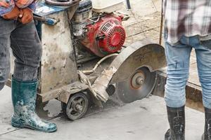 trabajador que utiliza una máquina de hoja de sierra de diamante cortando una carretera de hormigón en el sitio de construcción foto