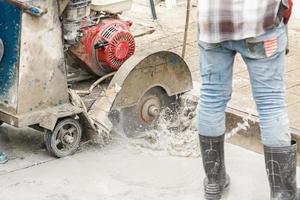 Worker using diamond saw blade machine cutting concrete road at construction site photo