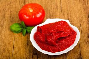 Tomato paste in a bowl on wooden background photo