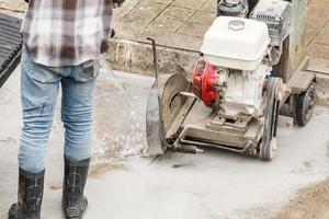 Worker using diamond saw blade machine cutting concrete road at construction site photo