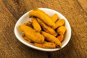 Tumeric roots in a bowl on wooden background photo
