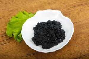 caviar negro en el plato y fondo de madera foto