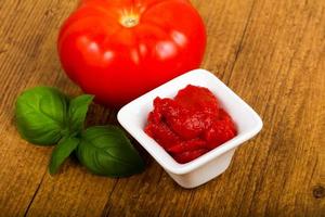 Tomato paste in a bowl on wooden background photo