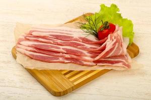 Raw bacon on wooden board and wooden background photo