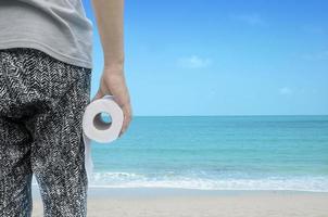 person holding toilet paper roll standing by the beach photo