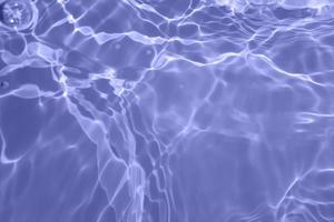 Defocus blurred transparent blue colored clear calm water surface texture with splash, bubble. Shining blue water ripple background. Surface of water in swimming pool. Blue bubble water shining. photo