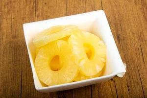 Canned pineapple in a bowl on wooden background photo