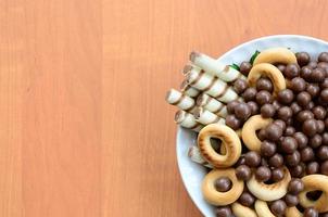 túbulos crujientes, bolas de fusión de chocolate y bagels yacen en un plato blanco sobre una mesa de madera. mezcla de varios dulces foto