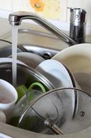 platos sucios y electrodomésticos de cocina sin lavar yacen en agua de espuma bajo un grifo de cocina foto