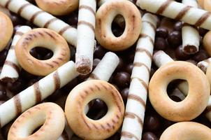 A lot of crispy sweet tubules, chocolate melting balls and yellow bagels lie on a wooden surface. Close up view photo