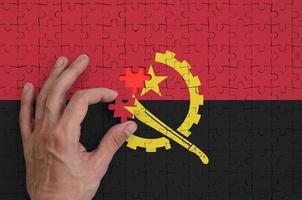 Angola flag  is depicted on a puzzle, which the man's hand completes to fold photo