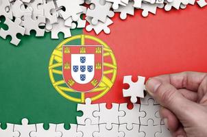 Portugal flag  is depicted on a table on which the human hand folds a puzzle of white color photo