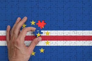 Cabo verde flag  is depicted on a puzzle, which the man's hand completes to fold photo