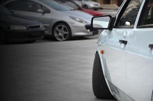 Diagonal view of a white glossy car that stands on a square of gray tiles photo