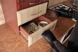 Robber in black outfit and gloves see in opened shelf in kitchen. The thief takes out the golden necklace from a shelf photo