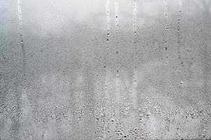 textura de una gota de lluvia sobre un fondo transparente húmedo de vidrio. tonificado en color gris foto