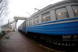 The railway track in a misty morning. The Ukrainian suburban train is at the passenger station. Fisheye photo with increased distortion