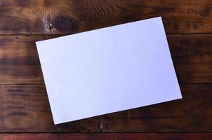 Photo of a clean white blank sheet of paper lie on a brown wooden background. Plenty of space for text