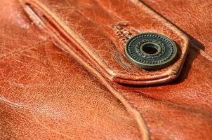 Brown leather texture. Useful as background for any design work. Macro photo of a button on outer clothing made of genuine leather