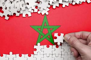Morocco flag  is depicted on a table on which the human hand folds a puzzle of white color photo