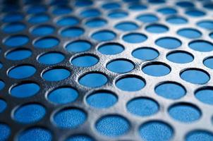 Black metal computer case panel mesh with holes on blue background. Abstract close up image photo