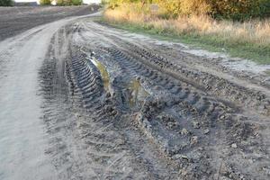 Autumn landscape with a curved road and traces of the tread of large wheels of agricultural machinery photo