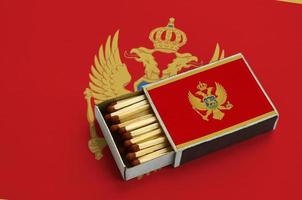 Montenegro flag  is shown in an open matchbox, which is filled with matches and lies on a large flag photo