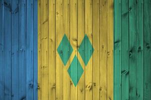 Saint Vincent and the Grenadines flag depicted in bright paint colors on old wooden wall. Textured banner on rough background photo