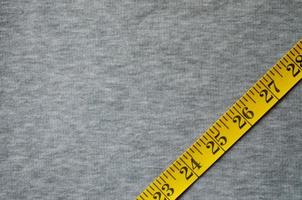 Yellow measuring tape lies on a gray knitted fabric photo