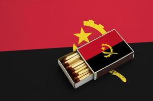 la bandera de angola se muestra en una caja de fósforos abierta, que está llena de fósforos y se encuentra en una bandera grande foto