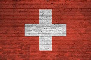 Switzerland flag depicted in paint colors on old brick wall. Textured banner on big brick wall masonry background photo