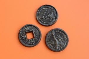 Three chocolate products in the form of Euro, USA and Japan coins lie on an orange plastic background. A model of cash coins in an edible form photo