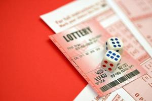 Red lottery ticket with dice lies on pink gambling sheets with numbers for marking to play lottery. Lottery playing concept or gambling addiction. Close up photo