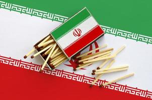 Iran flag  is shown on an open matchbox, from which several matches fall and lies on a large flag photo