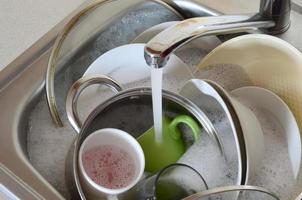 Dirty dishes and unwashed kitchen appliances lie in foam water under a tap from a kitchen faucet photo