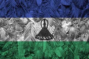 Lesotho flag depicted on many leafs of monstera palm trees. Trendy fashionable backdrop photo