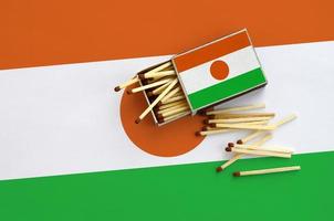 Niger flag  is shown on an open matchbox, from which several matches fall and lies on a large flag photo