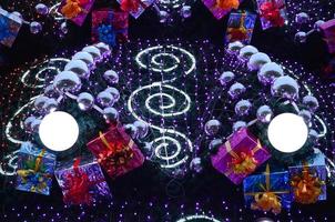 A fragment of a huge Christmas tree with many ornaments, gift boxes and luminous lamps. Photo of a decorated Christmas tree close-up