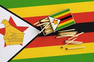 Zimbabwe flag  is shown on an open matchbox, from which several matches fall and lies on a large flag photo