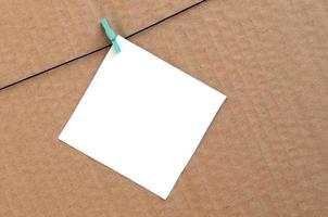 White blank card on rope on a brown cardboard background. Creative reminder, small sheet of paper on wooden clothespin, memo backdrop photo