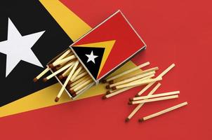 Timor Leste flag  is shown on an open matchbox, from which several matches fall and lies on a large flag photo