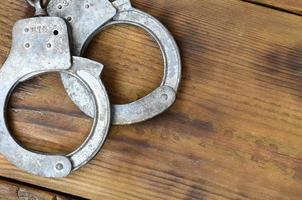 Old and rusty police handcuffs lie on a scratched wooden surface. The concept of an old crime photo