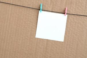 White blank card on rope on a brown cardboard background. Creative reminder, small sheet of paper on wooden clothespin, memo backdrop photo