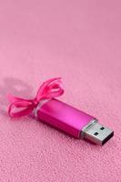 Brilliant pink usb flash memory card with a pink bow lies on a blanket of soft and furry light pink fleece fabric. Classic female gift design for a memory card photo